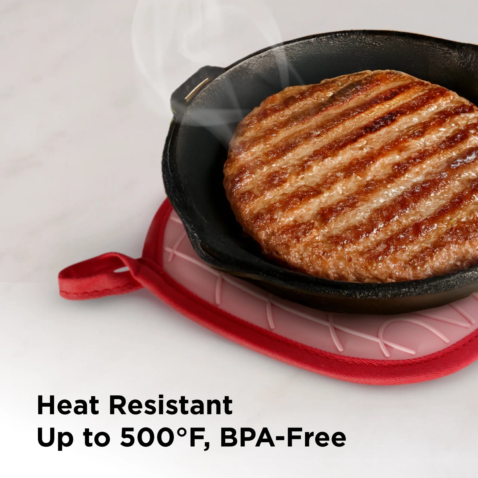 A red silicone pot holder placed under a steaming hot cast iron skillet with a grilled burger patty. Text highlights: "Heat Resistant – Up to 500°F, BPA-Free."